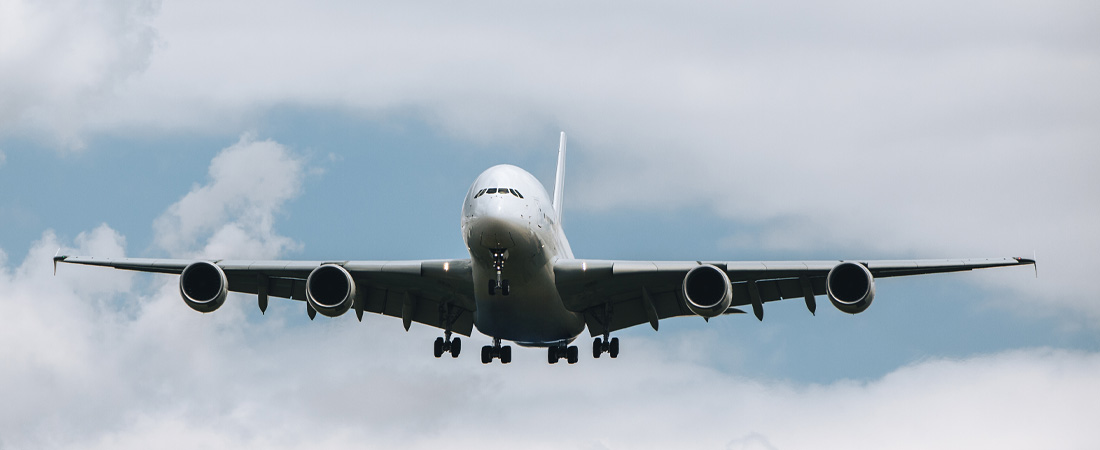 Vista frontal de un avión en pleno vuelo con un cielo parcialmente nublado de fondo.
