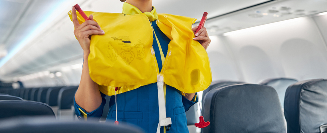 Miembro de la tripulación de cabina mostrando cómo ponerse el chaleco salvavidas amarillo inflable en el pasillo del avión.