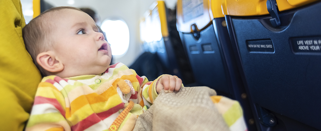 Primer plano de un bebé con ropa de rayas amarillas sentado en el asiento de un avión mirando hacia arriba.